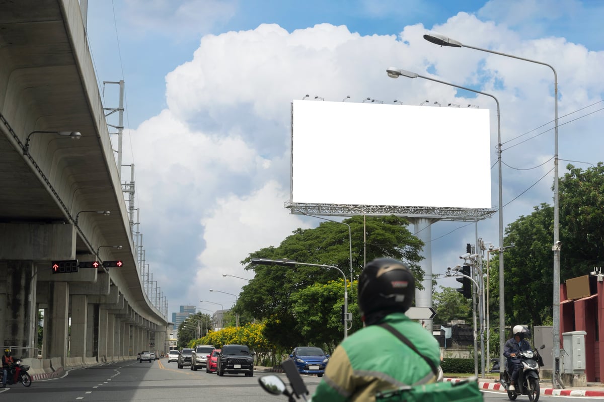 Empty billboard frame above a busy multi-lane city road with traffic and motorbikes under a blue sky