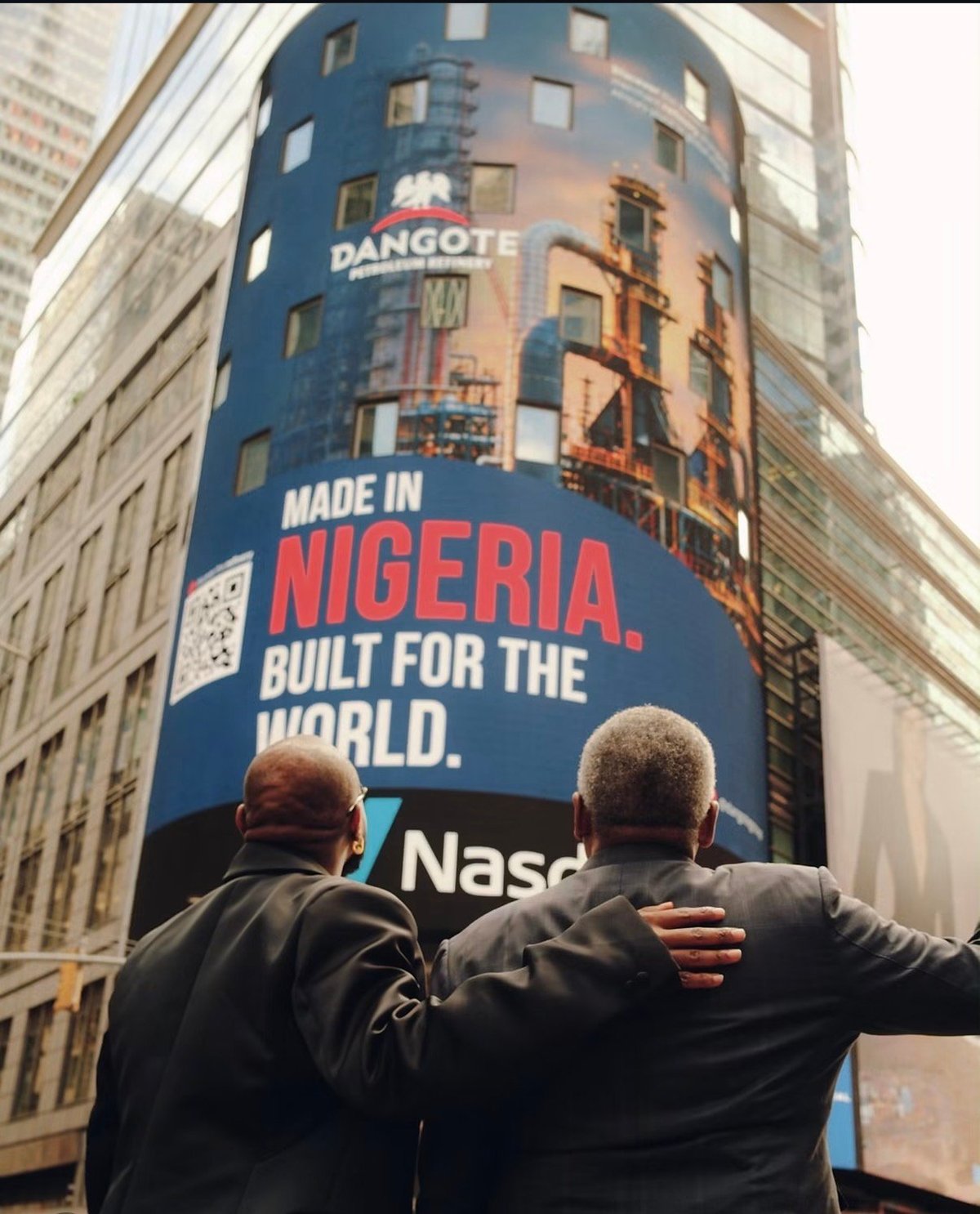 Two men viewing a large blue billboard displaying Made in Nigeria Built for the World message with Dangote branding on an urban street